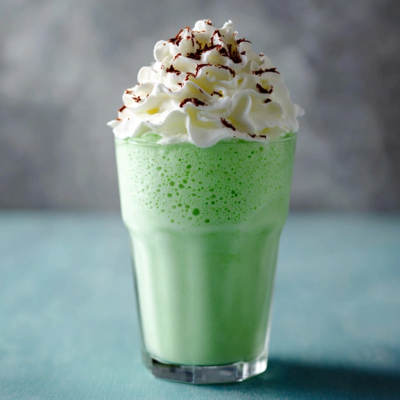 A glass of green milk with whipped cream.