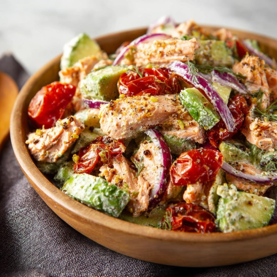A bowl of salad with chicken, tomatoes, onions, and avocado.