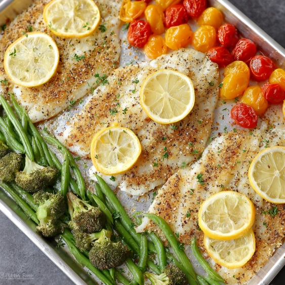A pan of food with fish, broccoli, and lemon slices.