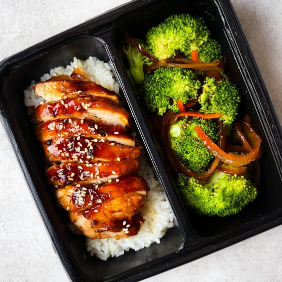 A black plastic container with rice and broccoli.