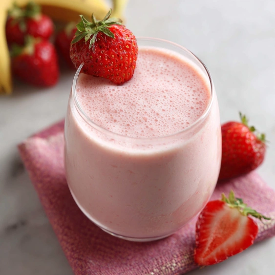 A glass of pink milk with a strawberry on top.