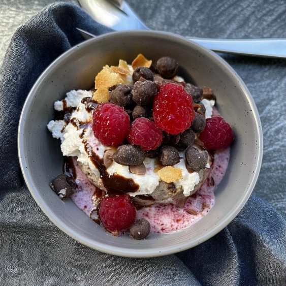 A bowl of ice cream with chocolate and raspberries.