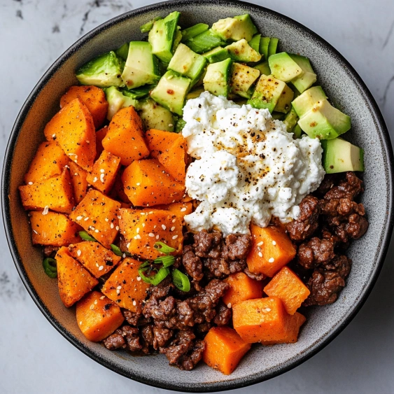 A bowl of food with meat, cheese, and vegetables.