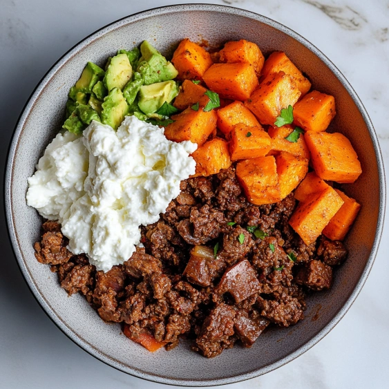 A bowl of food with meat, avocado, and carrots.