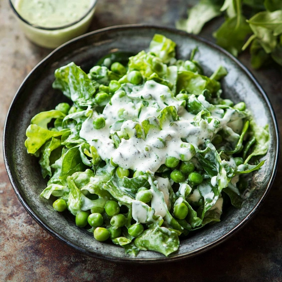 A bowl of salad with peas and dressing.