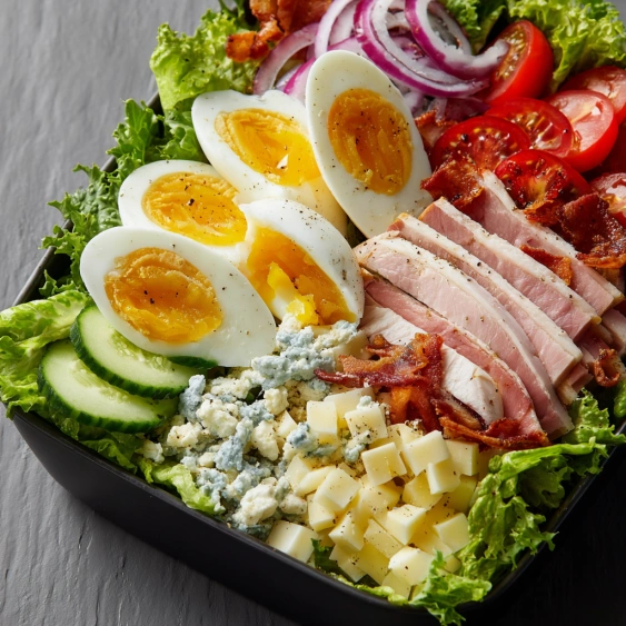 A salad with eggs, bacon, tomatoes, onions and lettuce.